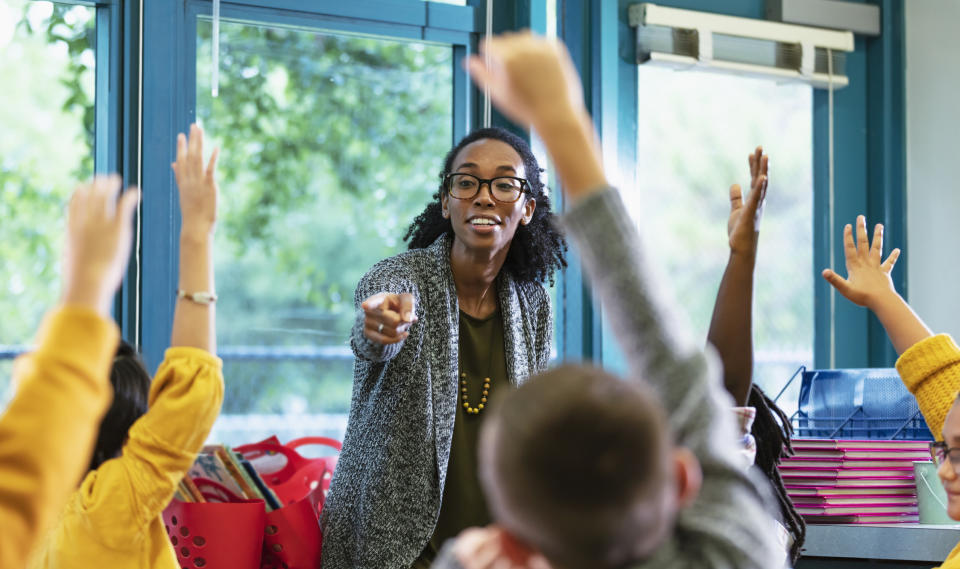 A teacher pointing at a student as they all raise their hands