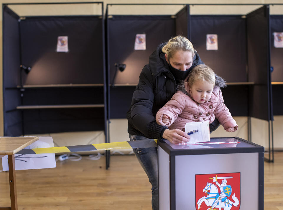 A woman wearing a face mask to protect against the coronavirus, with a child, casts her ballot at a polling station during the second round of a parliamentary election in Vilnius, Lithuania, Sunday, Oct. 25, 2020. Polls opened Sunday for the run-off of national election in Lithuania, where the vote is expected to bring about a change of government following the first round, held on Oct. 11, which gave the three opposition, center-right parties a combined lead. (AP Photo/Mindaugas Kulbis)