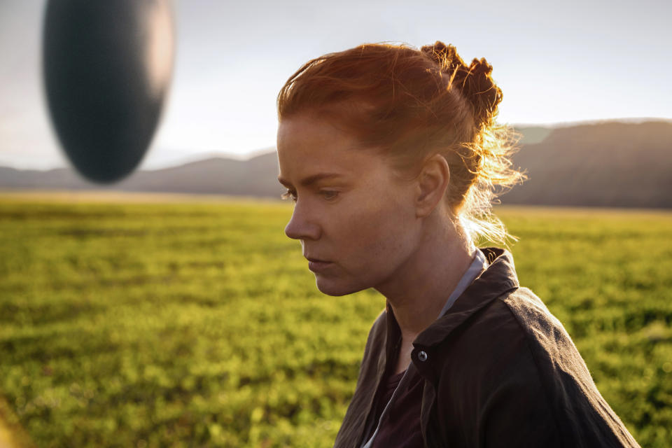 Amy Adams gazes thoughtfully in a scene from "Arrival," with an alien spacecraft hovering in the distance over a field