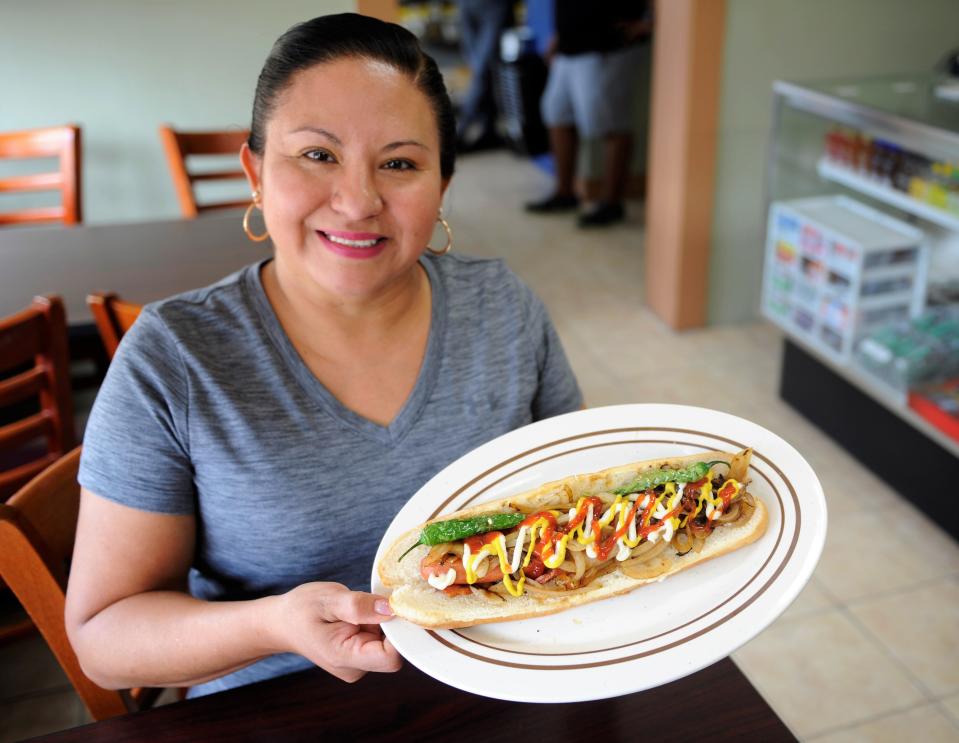 Fabiola Nicolas serves a street hot dog--a footlong dog wrapped in bacon with griddled onions, ketchup, mustard, mayonnaise, and fried serrano chilies, at the Bodega Market, Luncheria & Grocery on Monday, Aug. 22, 2023.