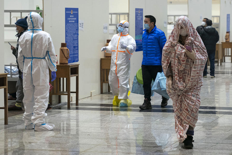 In this Wednesday, Feb. 5, 2020, photo, medical workers in a protective suit help patients who diagnosed with the coronaviruses as they arrive at a temporary hospital which transformed from an exhibition center in Wuhan in central China's Hubei province. Ten more people were sickened with a new virus aboard one of two quarantined cruise ships with some 5,400 passengers and crew aboard, health officials in Japan said Thursday, as China reported 73 more deaths and announced that the first group of patients were expected to start taking a new antiviral drug. (Chinatopix via AP)