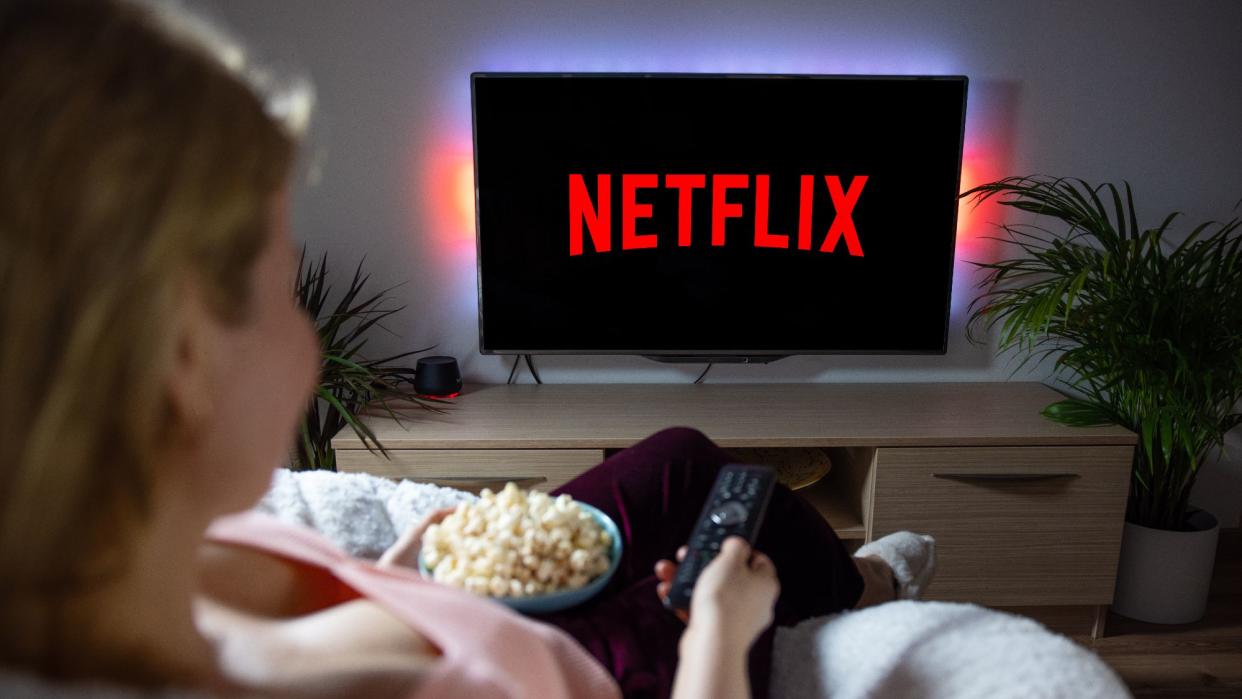  Woman with popcorn bowl holding remote to watch Netflix on television. 