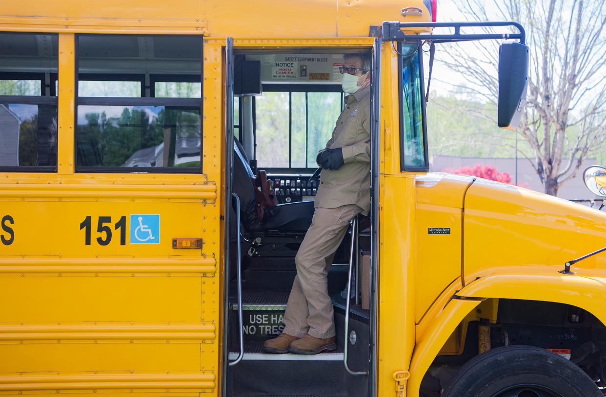 Dan Smith, an employee of the City of Asheville, stands on the steps of a meal school bus as he assists in delivering meals to children that attend Buncombe County Schools at the Hawthorne at Southside apartment complex on April 9, 2020.