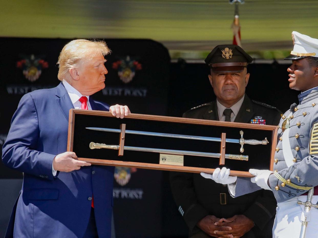 Donald Trump accepts a class gift at West Point during the graduation ceremony that saw him stagger awkwardly down a ramp: EPA