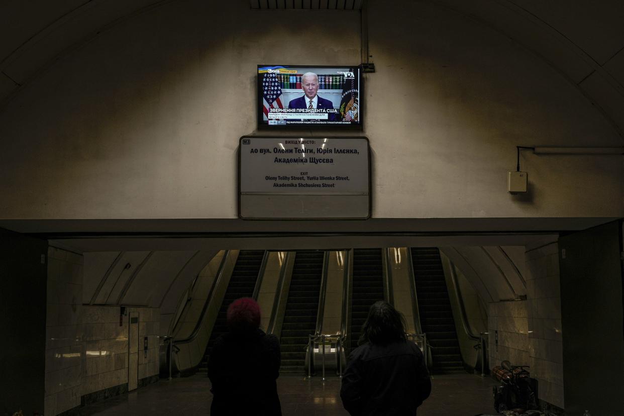 Two women watch U.S. President Joe Biden making statements on a news channel in a subway station turned into a shelter in Kyiv, Ukraine, Tuesday, March 8, 2022.