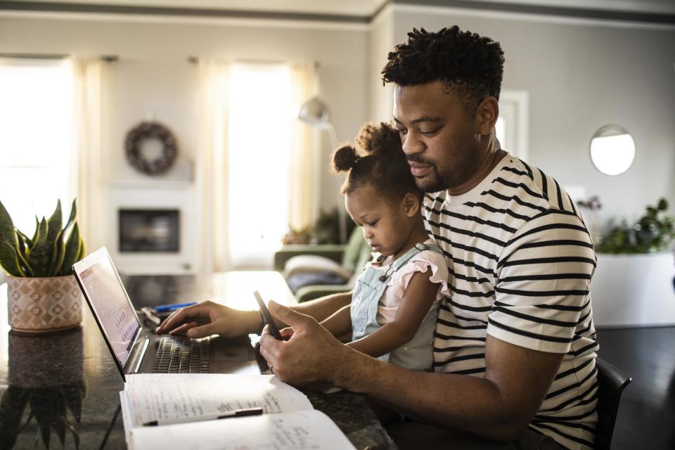 Father working from home while holding toddler