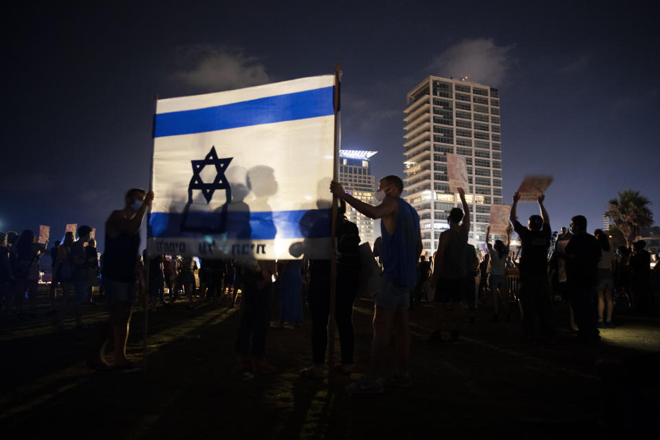 Protesters hold the Israeli national flag during a protest against Israel's Prime Minister Benjamin Netanyahu in Tel Aviv, Israel, Saturday, July 25, 2020. Protesters demanded that the embattled Israeli leader resign as he faces a trial on corruption charges and grapples with a deepening coronavirus crisis. (AP Photo/Oded Balilty)