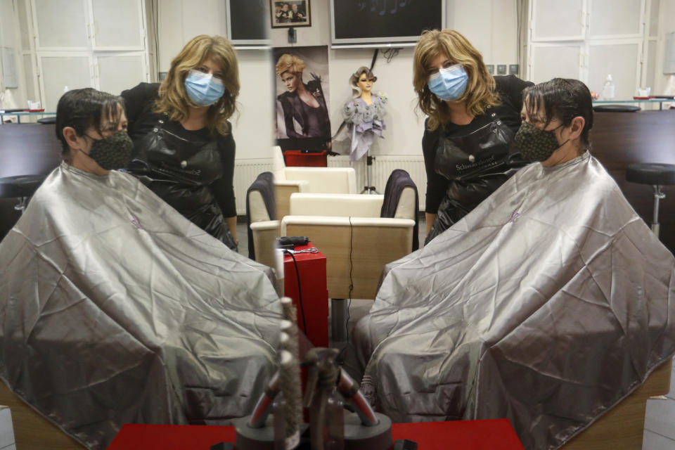 Hairdresser Andrea Roder is reflected in a mirror while posing with a customer in Budapest, Hungary, Wednesday April 7, 2021. Hungary's government lifted several lockdown restrictions on Wednesday, even as some doctors and medical experts urged caution after a record-breaking day of COVID-19 deaths, a move that came as Hungary reached 2.5 million first-dose vaccinations, a benchmark the government set for when a gradual reopening could move forward. (AP Photo/Laszlo Balogh)