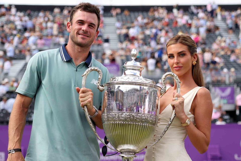 <p>Clive Brunskill/Getty</p> Tommy Paul and Paige Lorenze pose for a photo with the cinch Championships 2024 winners trophy on Day Seven of the cinch Championship at The Queen
