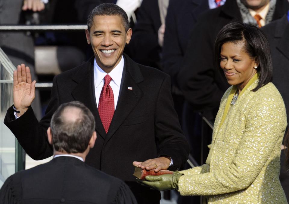 barack obama raises his right hand as his left hand rests on a bible that michelle obama holds for his inauguration, both are looking at supreme court justice john roberts