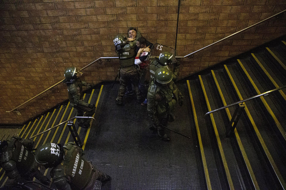 Chilean Carabineros separate two men who were fighting during a student protest against the rising cost of subway and bus fare, in Santiago, Friday, Oct. 18, 2019. (AP Photo/Esteban Felix)