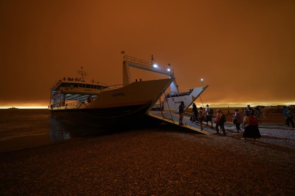 People use a ferry to evacuate from Pefki village on Evia island, about 189 kilometers (118 miles) north of Athens, Greece, Sunday, Aug. 8, 2021. Pillars of billowing smoke and ash are blocking out the sun above Greece's second-largest island as a days-old wildfire devours pristine forests and triggers more evacuation alerts. (AP Photo/Petros Karadjias)