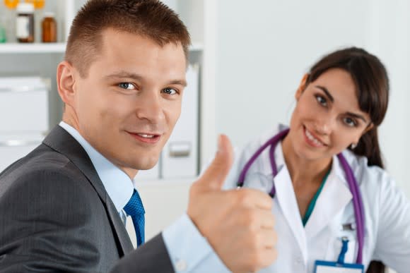 Businessman giving thumbs up as smiling doctor sits nearby.