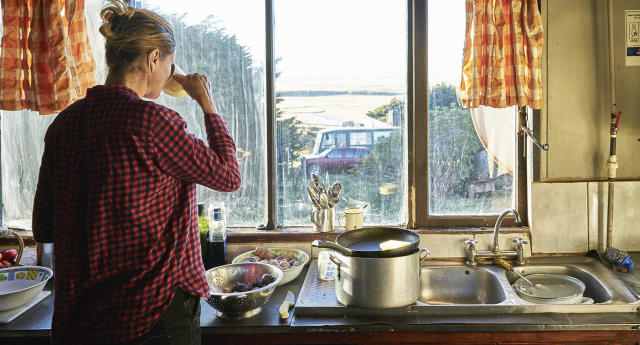 Woman standing in kitchen preparing meal and drinking from cup