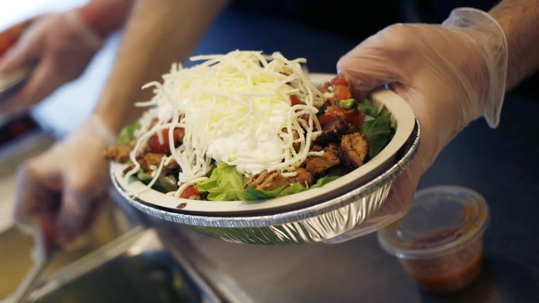Close-up of Chipotle employee's hands holding a prepared burrito bowl