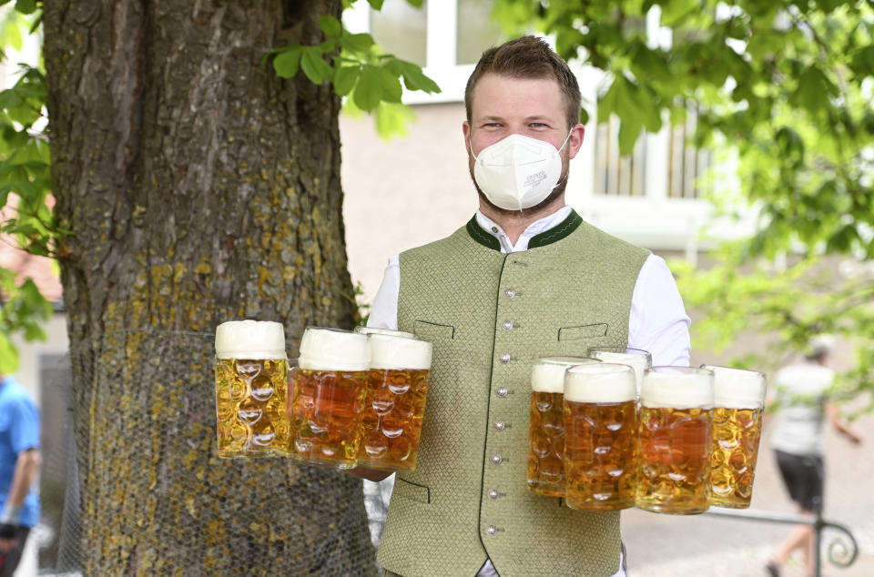 A waiter with face covering protection carries glasses of beer for customers in the beer garden at the "Gasthof zur Br'cke" during a press event for the opening of the beer garden season, in Kaufering, Germany, Monday May 10, 2021. As of May 10, outdoor restaurants are allowed to reopen in Bavarian counties and cities. (Tobias Hase/dpa via AP)