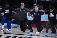 Phoenix Suns head coach Monty Williams, center left, and Philadelphia 76ers head coach Brett Brown, center right, kneel during the national anthem prior to the start of an NBA basketball game Tuesday, Aug. 11, 2020, in Lake Buena Vista, Fla. (AP Photo/Ashley Landis, Pool)