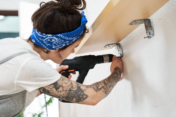 a woman drilling a shelf to the wall