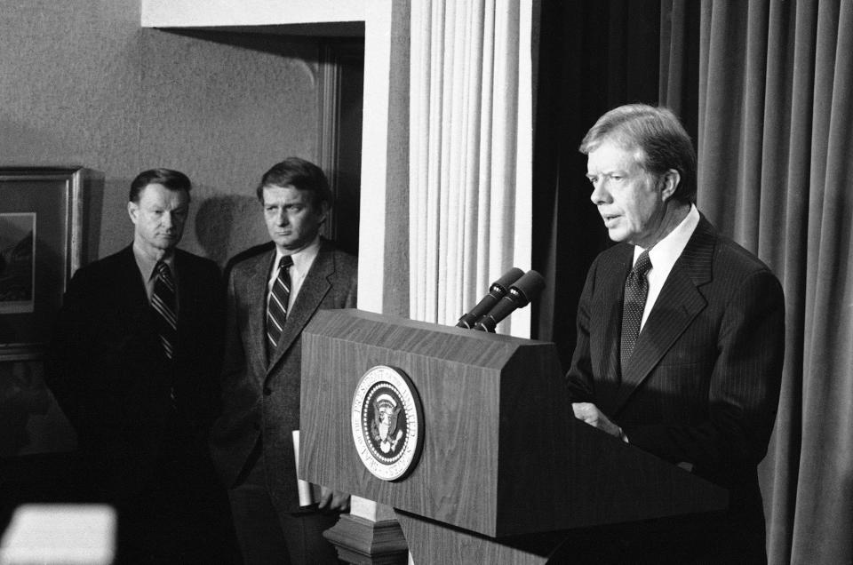 Zbigniew Brzezinski looks on as Pres. Carter faces reporter, Dec. 28, 1979