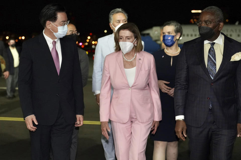 Nancy Pelosi walks on an airport tarmac surrounded by a half dozen others, all wearing face masks.
