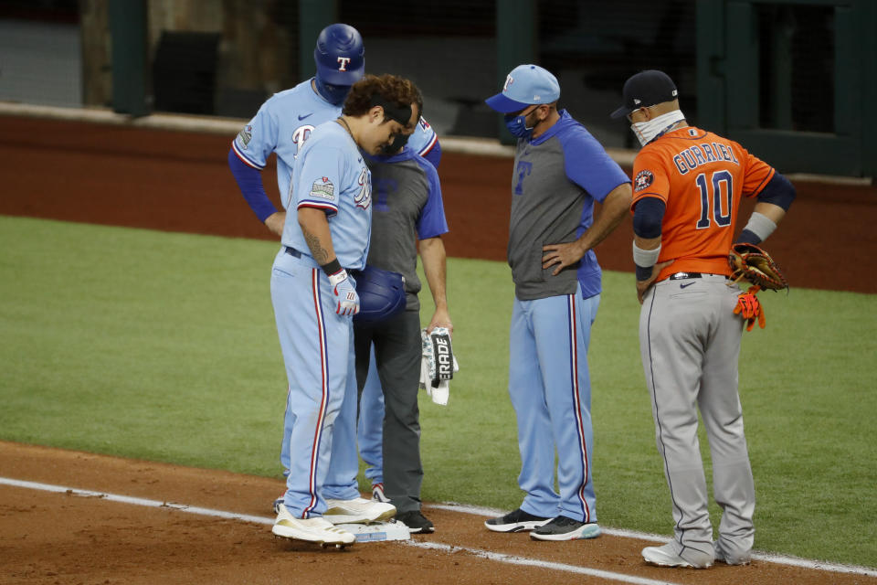 Texas Rangers' Shin-Soo Choo, left, is examined after falling at first base while trying to beat a throw while manager Chris Woodward, center, and Houston Astros first baseman Yuli Gurriel (10) standby during the first inning of a baseball game in Arlington, Texas, Sunday, Sept. 27, 2020. (AP Photo/Roger Steinman)