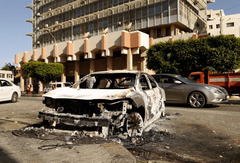 The remains of a car damaged in clashes remains on a street in the Libyan capital of Tripoli on Sunday, August 28 2022. Deadly clashes broke out Saturday in Libya's capital between militias backed by its two rival administrations, portending a return to violence amid a long political stalemate. (AP Photo/Yousef Murad)