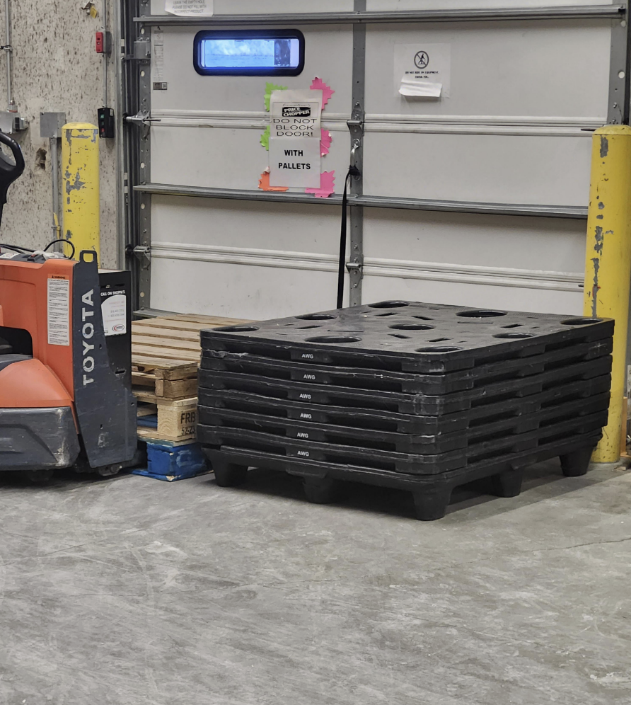 Stacks of pallets in front of a warehouse door under a "Do not block doors with pallets" sign