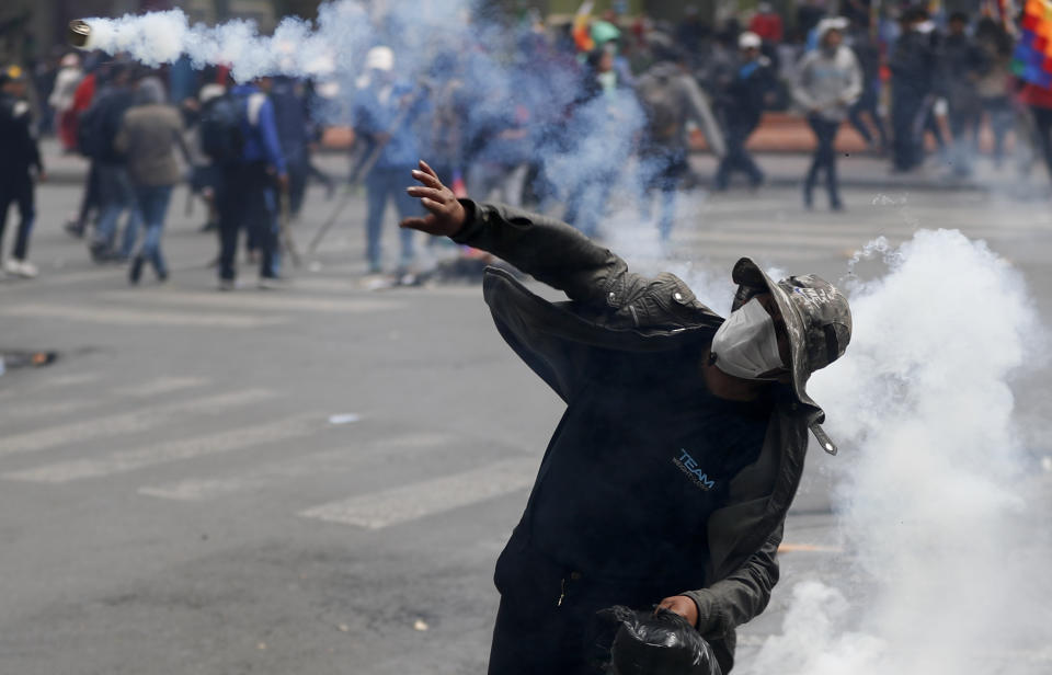 A backer of former President Evo Morales throws back a tear gas canister at police during clashes in La Paz, Bolivia, Wednesday, Nov. 13, 2019. Bolivia's new interim president Jeanine Anez faces the challenge of stabilizing the nation and organizing national elections within three months at a time of political disputes that pushed Morales to fly off to self-exile in Mexico after 14 years in power. (AP Photo/Natacha Pisarenko)