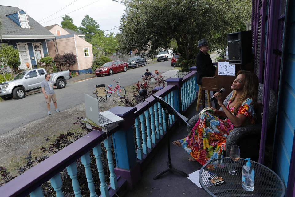 Anais St. John and pianist Harry Mayronne hold a front porch concert at her home in New Orleans, Saturday, April 11, 2020. With New Orleans music venues shuttered for more than a month now because of the coronavirus outbreak, musicians and fans are finding new places to connect – porches, living rooms, studios and lawns – and reaching their largest audiences online, many streaming performances live on social media platforms. But for the city's club owners awaiting the green light to reopen there's concern about all the uncertainties, like how long it may take tourists to return, how soon the music scene will rebound and when it does, what it will look like. (AP Photo/Gerald Herbert)