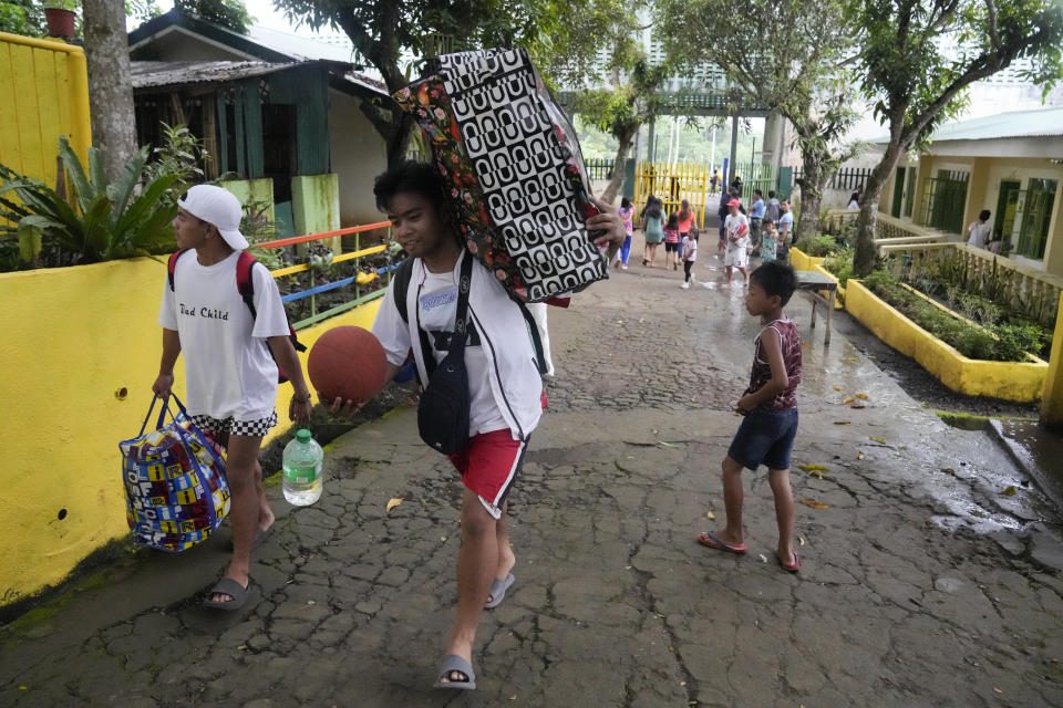 Evacuees carry their belongings as they arrive at a temporary relocation site at a school in Daraga town, Legaspi, Albay province, northeastern Philippines, Saturday, June 10, 2023. Monsoon rains that could be unleashed by an offshore typhoon were complicating worries of villagers threatened by restive Mayon volcano that has forced thousands of people to flee from their homes.(AP Photo/Aaron Favila)