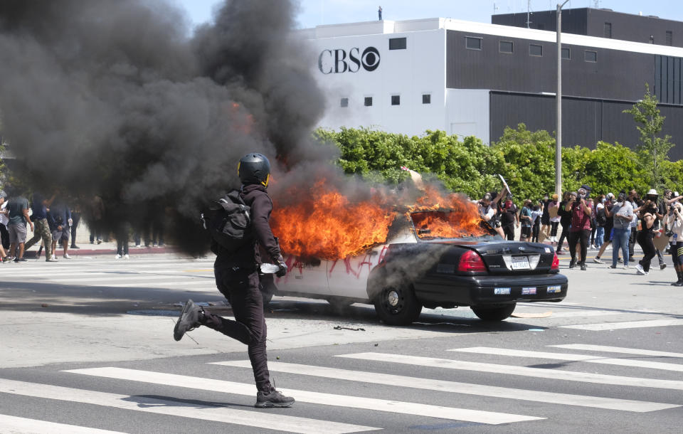Una persona corre mientras un vehículo policial arde, durante una protesta por la muerte de George Floyd en Los Ángeles, el sábado 30 de mayo de 2020. (AP Foto/Ringo H.W. Chiu)