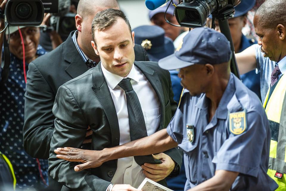 oscar pistorius walking into court with a guard holding him back with one arm