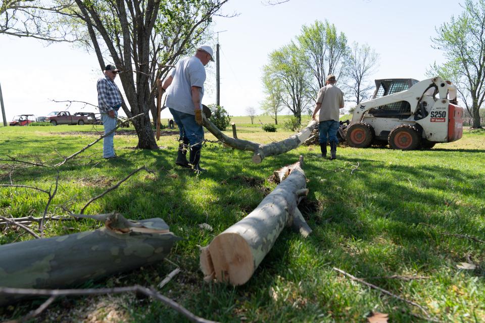 Neighbors help to clean up downed limbs Tuesday morning at Steve and Rae Colson's property in Overbrook.