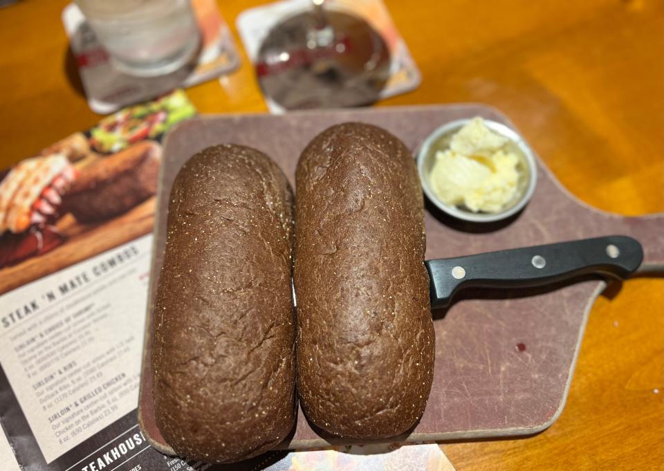 Two loaves of Brown bread on a cutting board next to a bowl of butter at an Outback Steakhouse