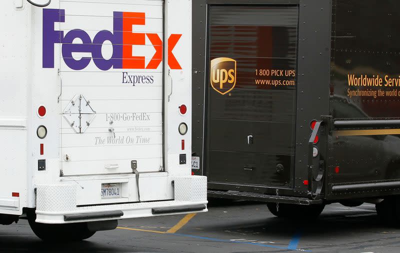 A FedEx truck is parked next to a UPS truck as both drivers make deliveries in downtown San Diego