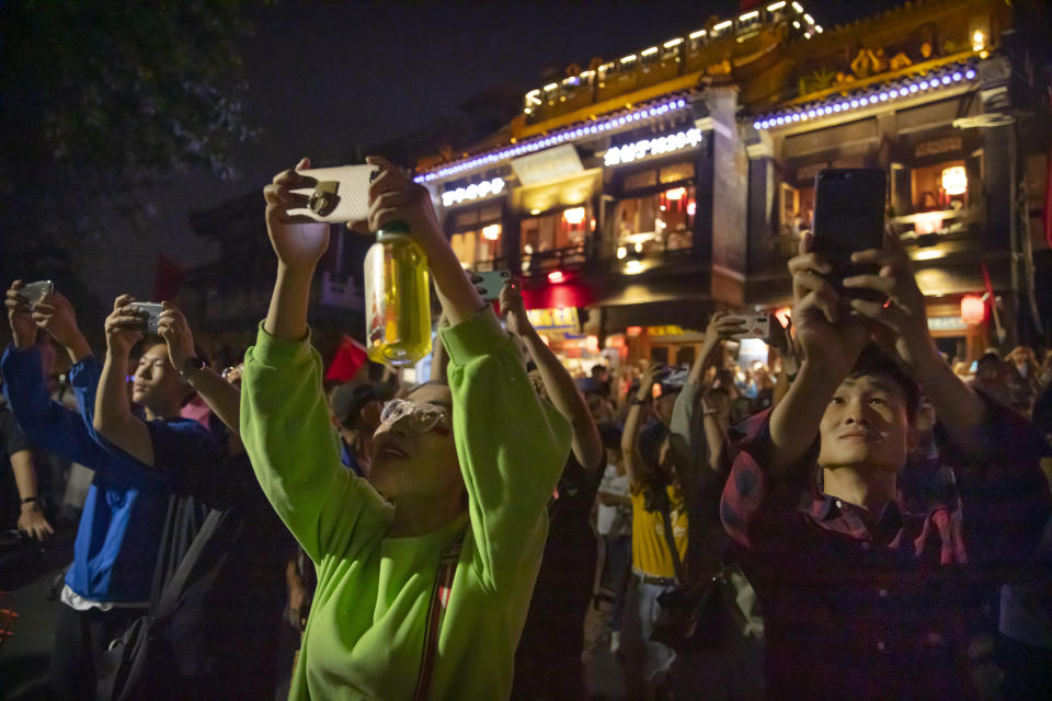 People use their smartphones to take photos at Qianhai Lake of fireworks in the distance at Tiananmen Square as part of a gala evening commemorating the 70th anniversary of the founding of Communist China in Beijing, Tuesday, Oct. 1, 2019. China's Communist Party marked 70 years in power with a military parade Tuesday that showcased the country's global ambitions while police in Hong Kong fought protesters in a reminder of strains at home. (AP Photo/Mark Schiefelbein)