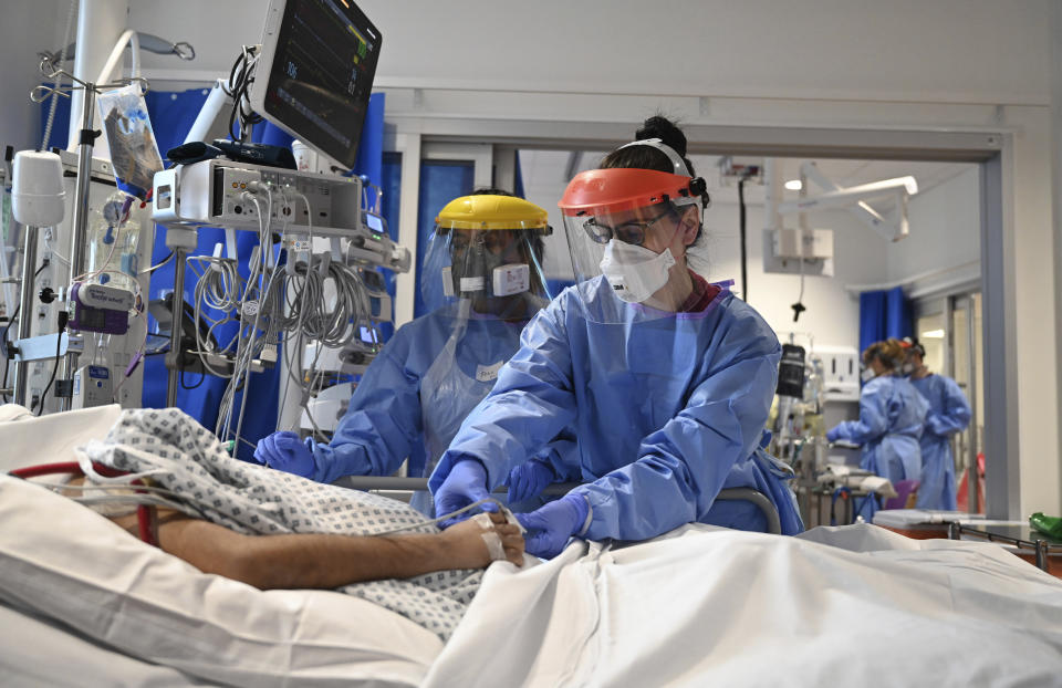 FILE - In this May 5, 2020 file photo members of the clinical staff wearing Personal Protective Equipment PPE care for a patient with coronavirus in the intensive care unit at the Royal Papworth Hospital in Cambridge, England. More than 100,000 people have died in the United Kingdom after contracting the coronavirus. That's according to government figures released Tuesday Jan. 26, 2021. Britain is the fifth country in the world to pass that mark, after the United States, Brazil, India and Mexico, and by far the smallest. (Neil Hall/Pool via AP, File)