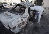 Authorities gather evidence from a burned-out car in Mughsha, Bahrain, Saturday, April 19, 2014. Authorities in Bahrain say an apparent car bombing has killed two people and wounded one west of the capital, Manama. Bahrain has been roiled by three years of unrest, with a Shiite-dominated opposition movement demanding greater political rights from the Sunni monarchy. (AP Photo/Hasan Jamali)