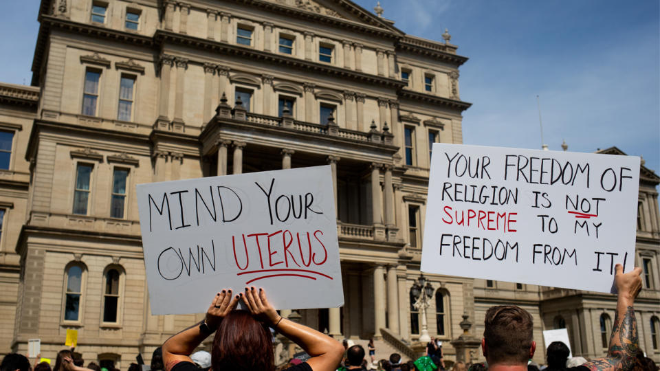 Abortion rights demonstrators hold signs reading: Mind your own uterus and Your freedom of religion is not supreme to my freedom from it.