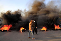 Protesters stand in front of burning tires that were set on fire to block a highway that links to the Beirut's international airport, during a protest against against the economic and financial crisis, in Beirut, Lebanon, Tuesday, March 2, 2021. The Lebanese pound has hit a record low against the dollar on the black market as the country's political crisis deepens and foreign currency reserves dwindle further. (AP Photo/Hussein Malla)