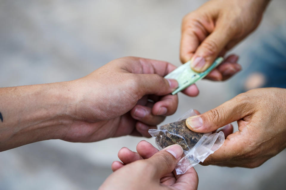 Two hands passing money and marijuana to another set of hands in an illegal marijuana transaction.