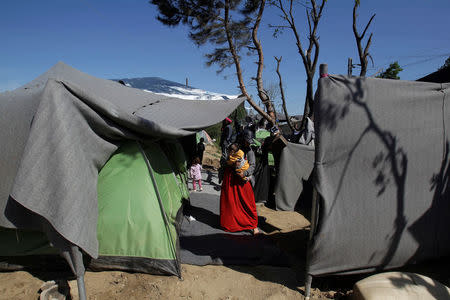 A woman holds her baby among tents at a makeshift camp for refugees and migrants at the Greek-Macedonian border near the village of Idomeni, Greece, April 12, 2016. REUTERS/Alexandros Avramidis