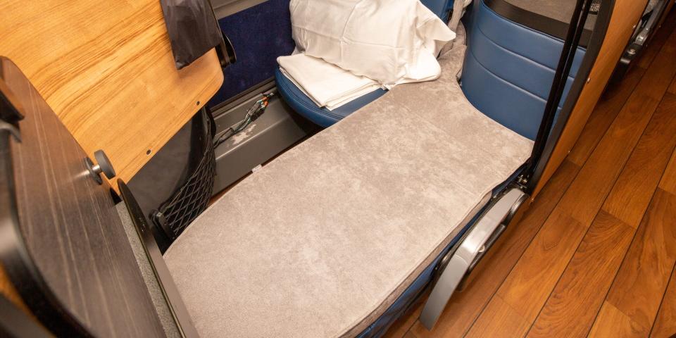 A flat grey bed next to a seat with a pillow.