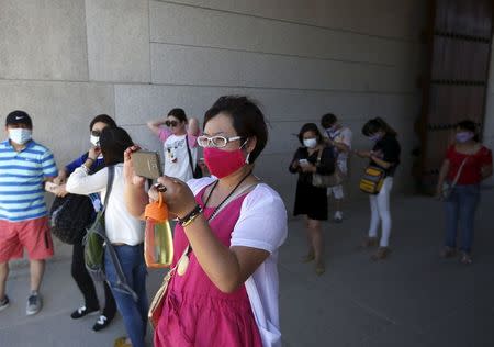 A Chinese tourist wearing a mask to prevent contracting Middle East Respiratory Syndrome (MERS) takes photographs as others rest in the shade of the main entrance of the Gyeongbok Palace in central Seoul, South Korea June 3, 2015. REUTERS/Kim Hong-Ji