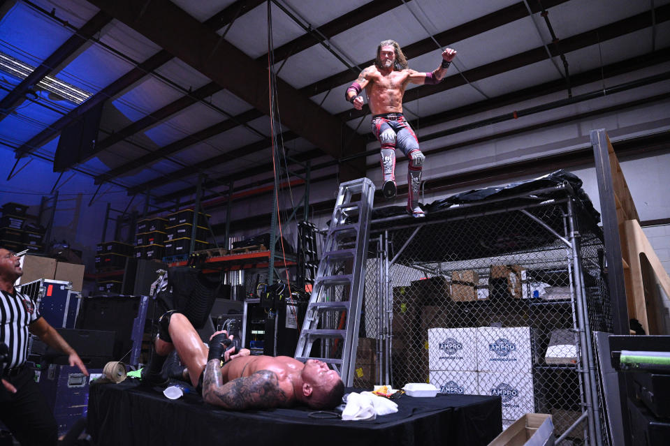 Edge uses an elbow drop to put Randy Orton through a table. (Photo Credit: WWE)