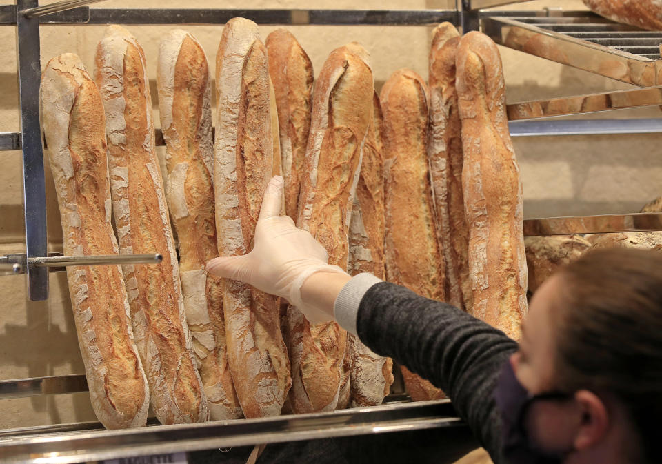 A vendor wearing a protective mask takes a baguette at a bakery in Paris, Monday, March 23, 2020. For most people, the new coronavirus causes only mild or moderate symptoms, such as fever and cough. For some, especially older adults and people with existing health problems, it can cause more severe illness, including pneumonia. (AP Photo/Michel Euler)