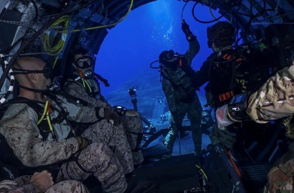 A group of US Marines sit underwater in the dry deck shelter of a US Navy submarine.