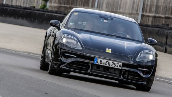 A black preproduction Porsche Taycan, an electric sports sedan, shown from the front on a test track.