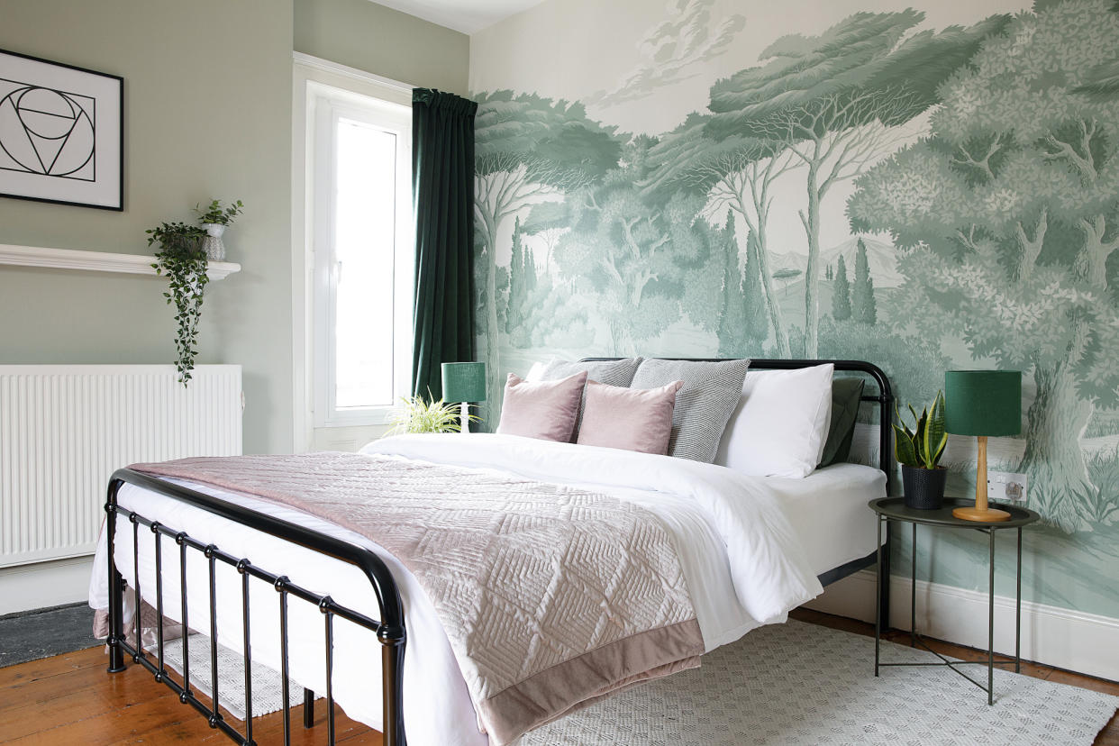  Bedroom with green walls, green nature-inspired wall mural, black metal bed, white rug and white and pink bedding 
