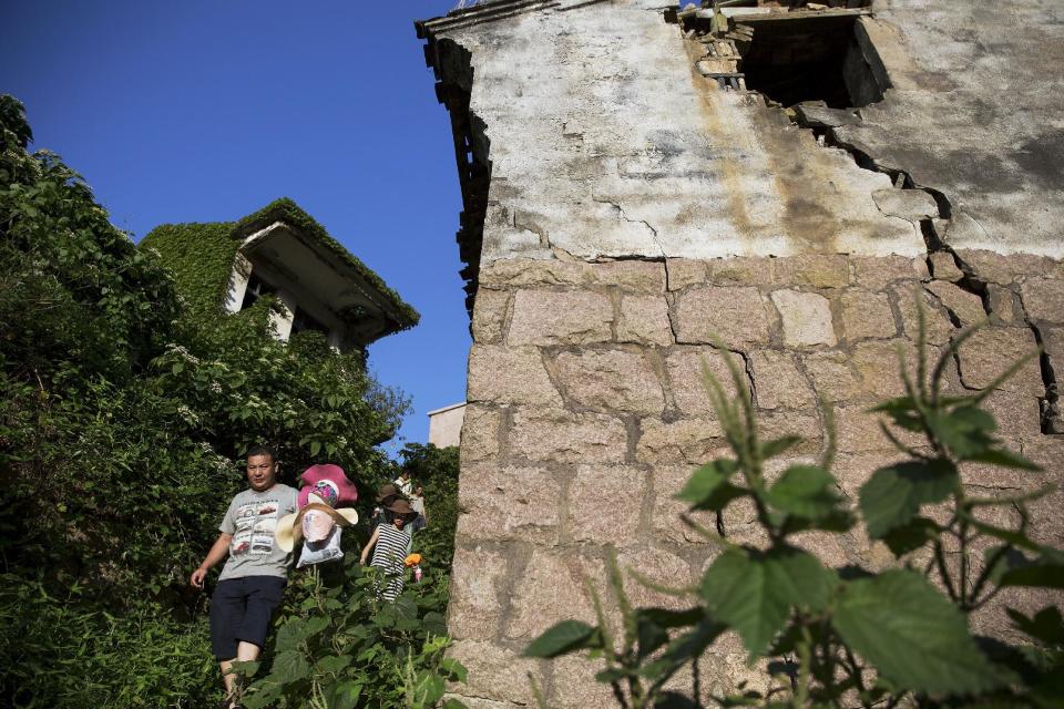 Tourists walk between buildings covered with leaves at the abandoned fishing village of Houtouwan on the island of Shengshan July 25, 2015. (REUTERS/Damir Sagolj)